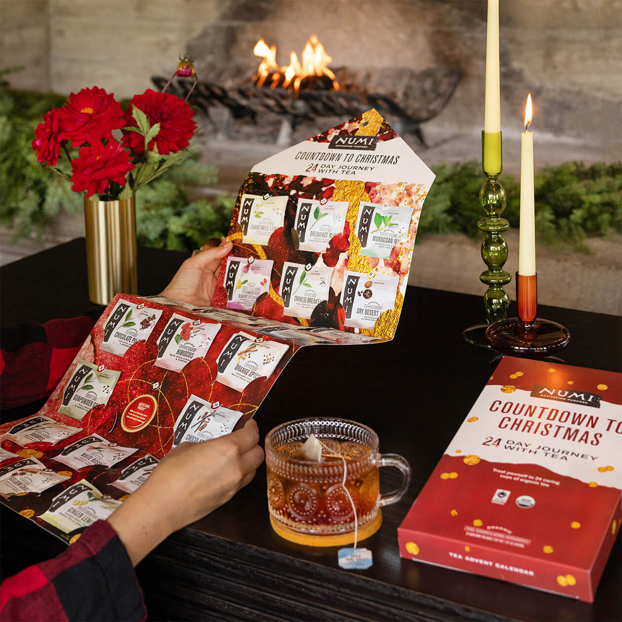 In a Christmas setting, a person holds up their Numi Advent Calendar and enjoys their tea