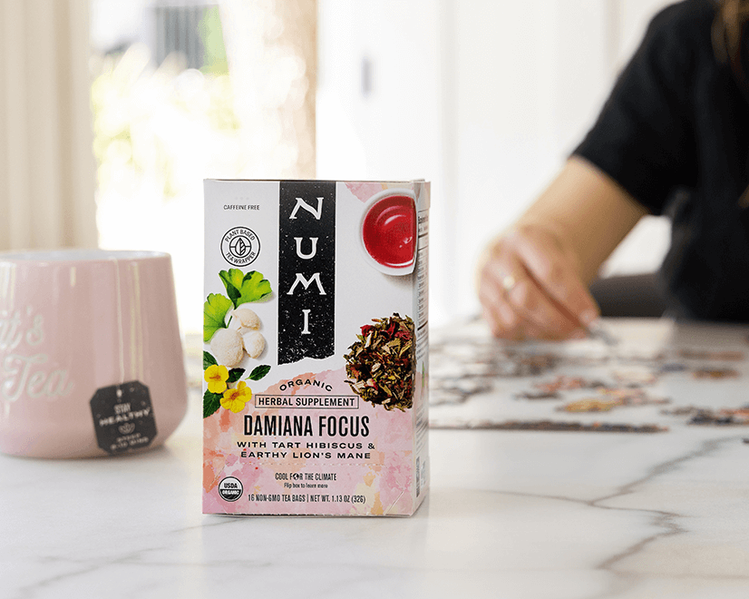 A woman working on a puzzle drinks Numi Damiana Focus tea