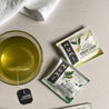 A cup of hot Ginger Lemon Tea on a linen background with a Ginger Lemon compostable tea bag wrapper