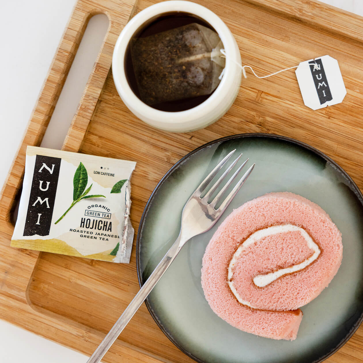 A cup of Hojicha tea brewing next to a pink dessert on a wood tray