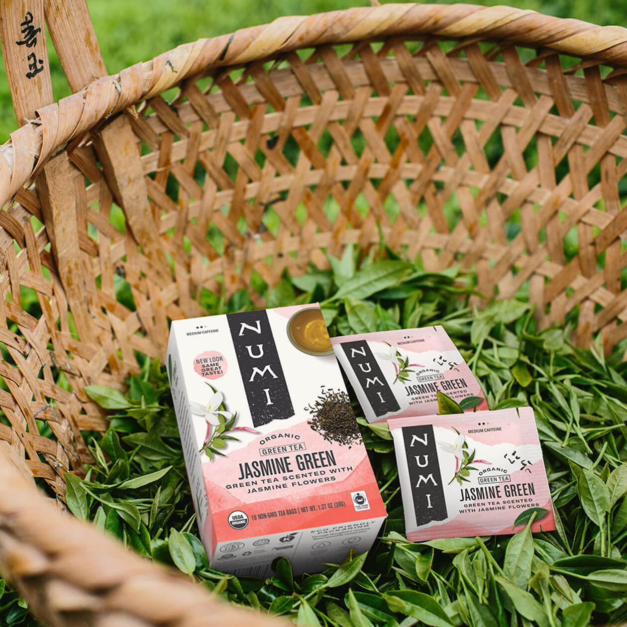 A box of Jasmine Green tea in a basket of freshly picked tea leaves