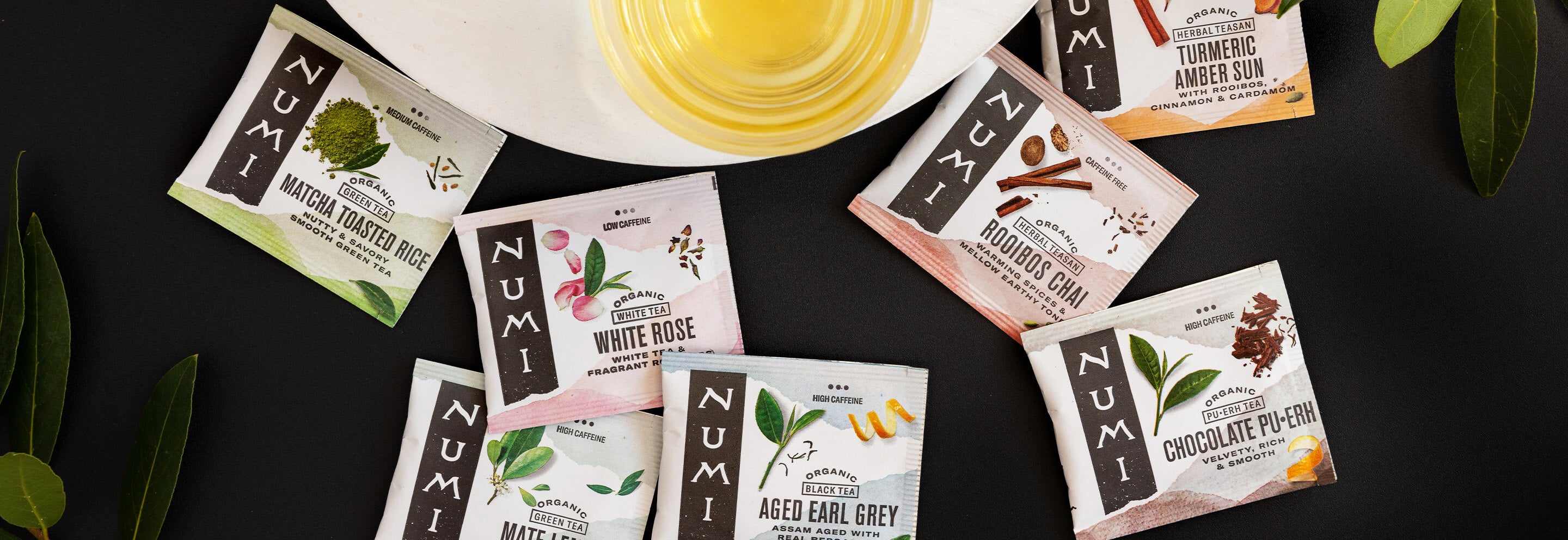 An assortment of Numi tea bag wrappers on a black background with a cup of tea