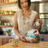 A woman in her kitchen opens her Tea By Mood gift and enjoys a hot cup of Mate Lemon